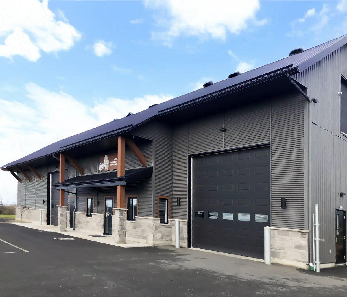 Bâtiment commercial industriel avec revêtement métallique gris, porte de garage noire et base en pierre sous ciel bleu