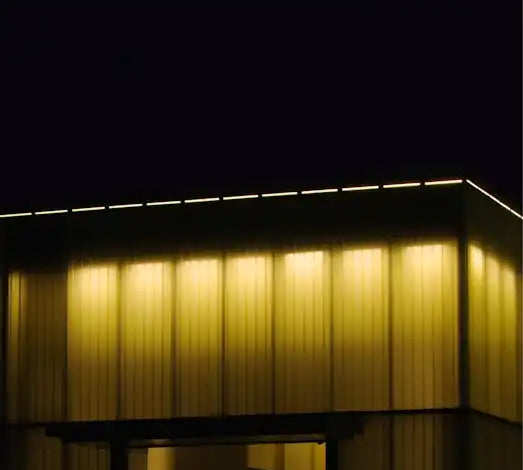 Bâtiment moderne à l'architecture cubique avec façade éclairée en jaune doré durant la nuit