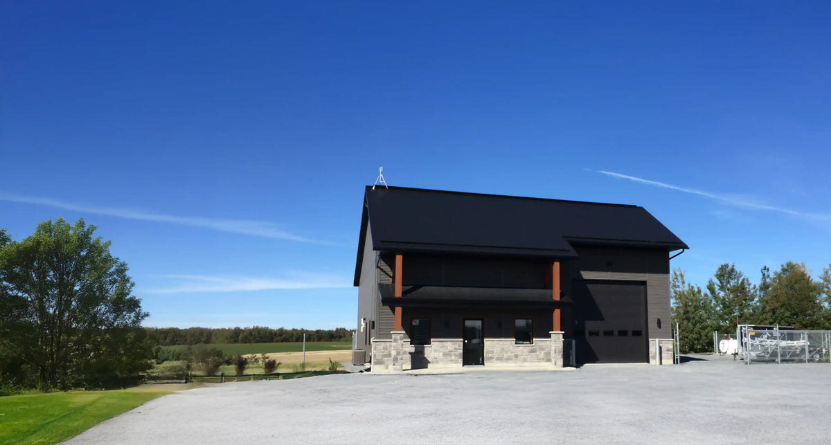 Bâtiment moderne noir à deux étages avec grande porte de garage et façade en pierre en milieu rural