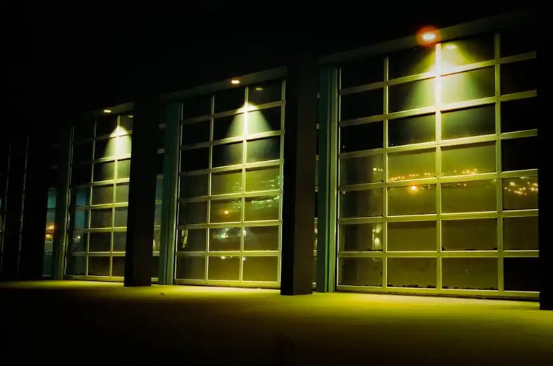 Façade vitrée d'un bâtiment moderne illuminée la nuit avec éclairage jaune et reflets urbains