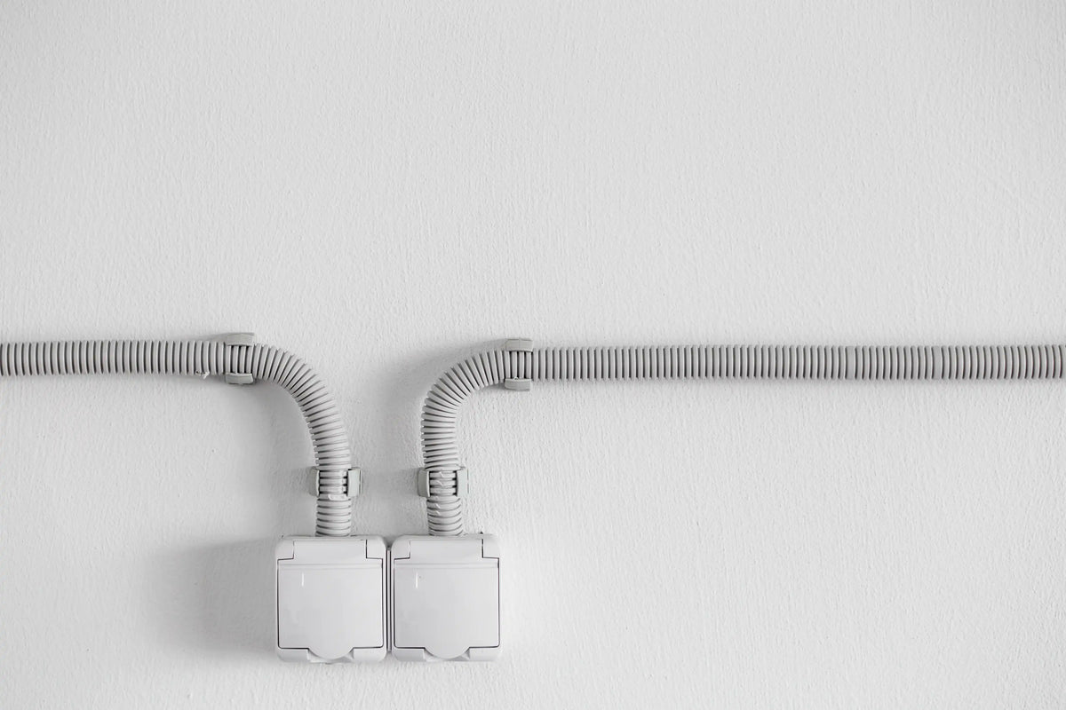Deux prises électriques blanches en saillie reliées par des gaines annelées sur un mur blanc